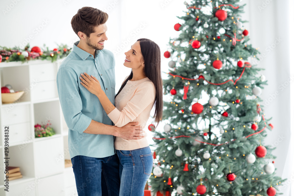Portrait of two people romantic spouses with brunet hair hugging enjoy christnas time x-mas vacation wearing blue denim jeans shirt pastel sweater in house with newyear decoration indoors