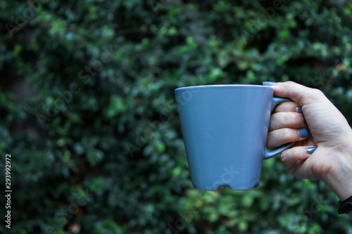 Mockup of female hand holding a coffee cup on natural garden background