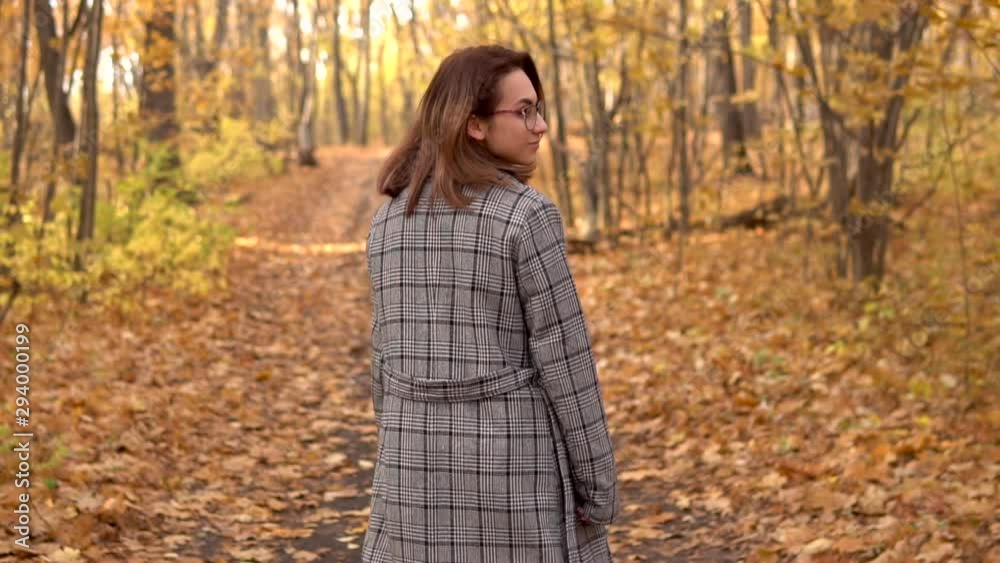 A young woman in glasses and a coat walks in the autumn forest. Yellow leaves around. Slow motion A young woman in glasses and a coat walks in the autumn forest. Yellow leaves around. Slow motion