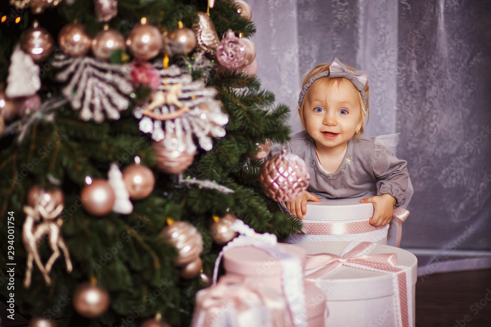 Little girl sitting under the Christmas tree. She hugs her hands Christmas gift boxes. The charming little girl sits under a Christmas tree with gifts. New Year's interior, holiday, Christmas.