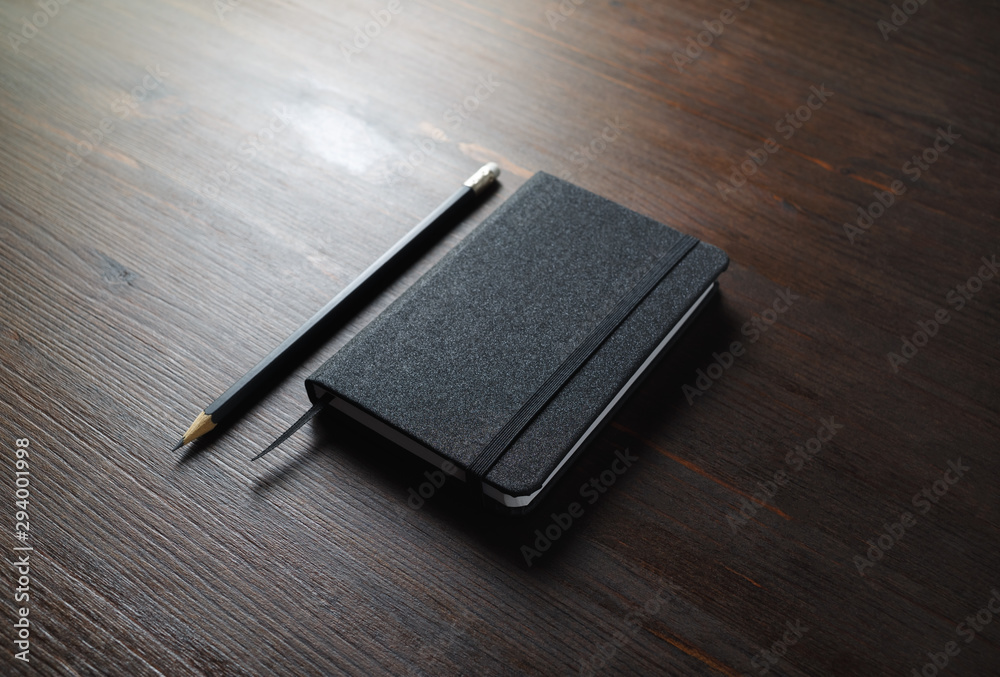 Black notebook and pencil on wooden background. Responsive design mockup. Black notebook and pencil on wooden background. Responsive design mockup.