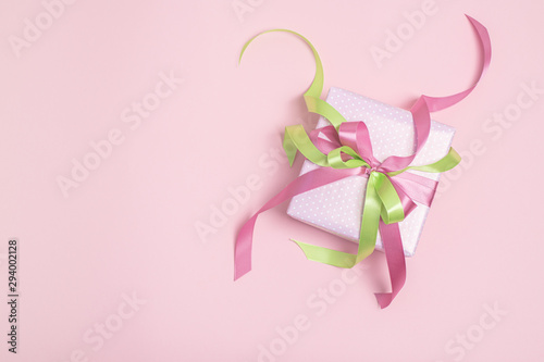 Gift box with green and pink ribbons on pink background with copy space. Holiday concept. Flat lay. 