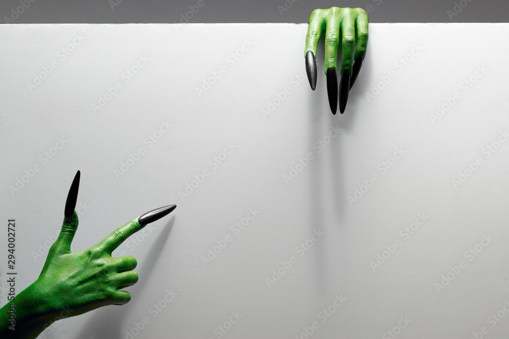 Fototapeta premium Halloween concept. Two green hands hold gray sheet of paper.