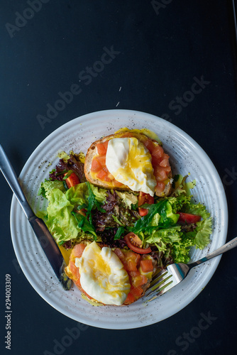Healthy breakfast. Toasts with salmon and poached egg, served with fresh salad on white plate on dark background. Place for inscription. Close-up. Space. Flat lay