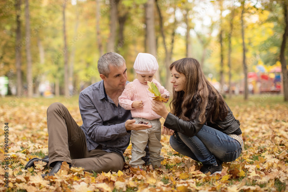 Happy married couple sitting on leaves in autumn and holding a beautiful baby daughter Happy married couple sitting on leaves in autumn and holding a beautiful baby daughter