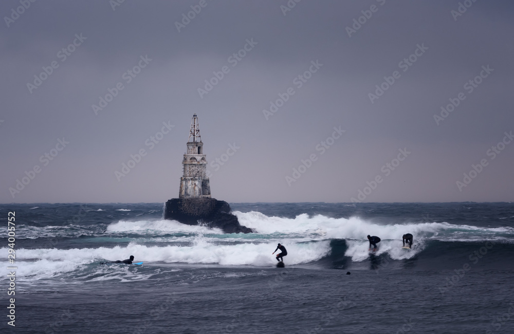 Big waves crashing at lighthouse. Dark and stormy weather at Ahtopol, Bulgaria and a surfer. Danger, dramatic scene.
