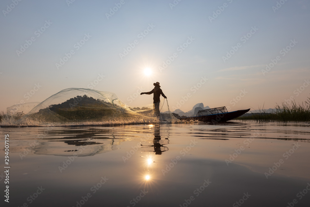 Asian fishermen throwing fishing net during sunset on wooden boat at the lake. Concept Fisherman's Lifestyle in countryside. Lopburi, Thailand, Asia