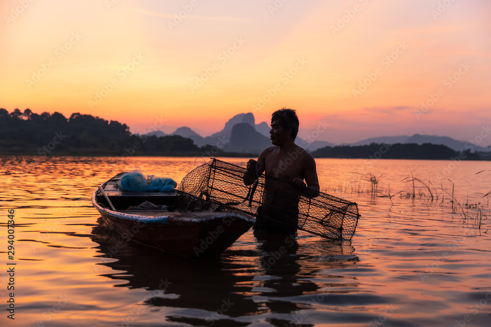Asian fisherman catching freshwater fish with fish trap rising out of the water during twilight at the lake. Concept Fisherman's Lifestyle in countryside. Lopburi, Thailand, Asia
