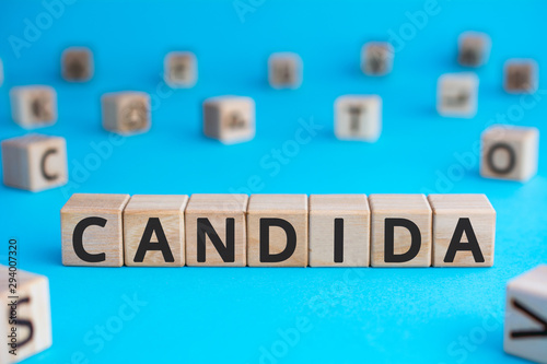 Candida - word from wooden blocks with letters, a parasitic fungus candida concept, random letters around, blue background