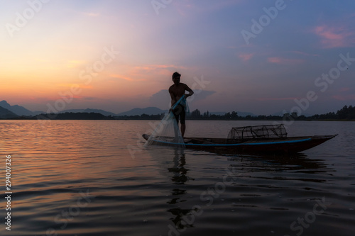 Asian fisherman catching freshwater fish in nature river with fishing Net on wooden boat during twilight. Concept Fisherman's Lifestyle in countryside. Lopburi, Thailand, Asia