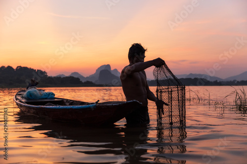 Asian fisherman catching freshwater fish with fish trap rising out of the water during twilight at the lake. Concept Fisherman's Lifestyle in countryside. Lopburi, Thailand, Asia