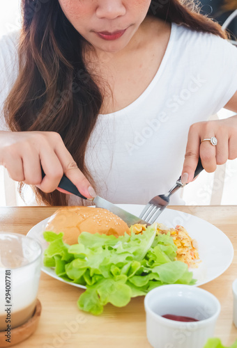 Eating breakfast omelette, bread, hamburger and vegetables on a white plate using a knife and fork