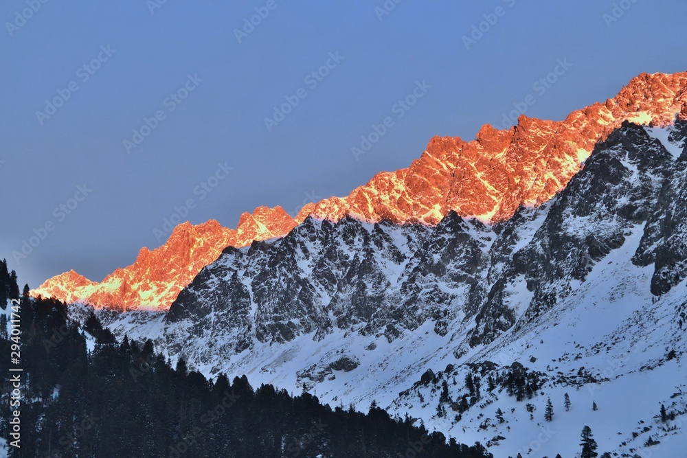 Beautiful sunset in Tatra mountains. High mountains covered with snow, orange sky, forest in the front.
