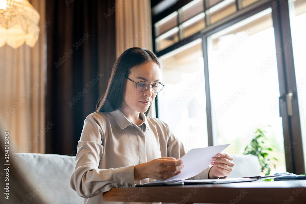 Serious brunette Asian female in smart casual reading documents before meeting Serious brunette Asian female in smart casual reading documents before meeting