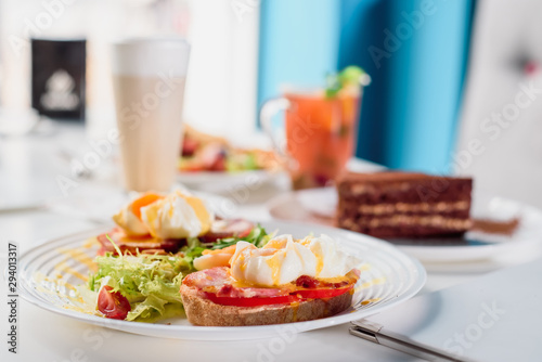 Toasts with ham, tomato and poached egg, served with fresh salad on white plate. Healthy breakfast on the table in the restaurant. Close-up. Space
