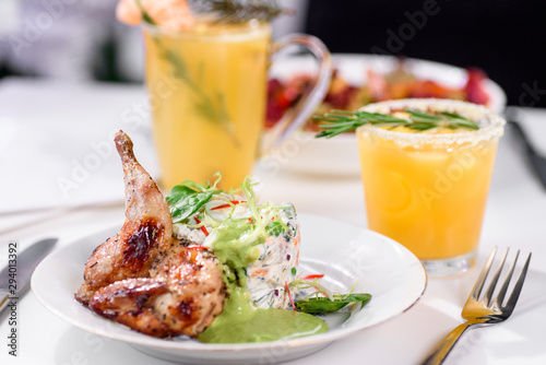 Tobacco chicken with salad on a white table in a restaurant. Tea and dessert on a blurred background. Large plna. Space
