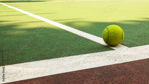 Yellow tennis ball hitting the sidelines on an green and orange artificial tennis court in the afternoon sun. sport background
