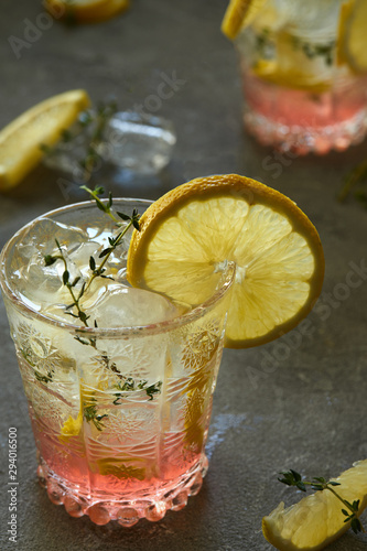 Cool drink with lemon and thyme in a glass on a gray background