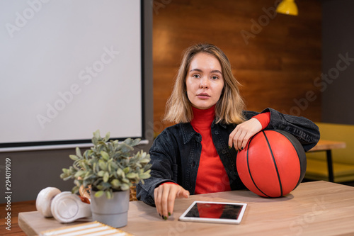 Pretty young casual student with ball and digital tablet sitting in college cafe