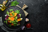 Salad: beetroot, pumpkin, corn and lettuce in a black plate on a black background. Top view. Free space for your text.