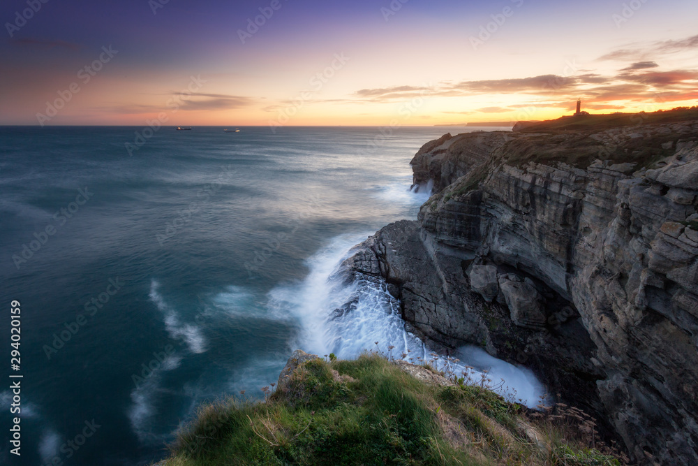 Sunrise view from a cliff in spain,near bilbao and santander, north atlantic coastline. Backlight sunlight lighting the ocean and harsh cliffs. Lighhouse in the backgrund. Very peaceful and calm mood.