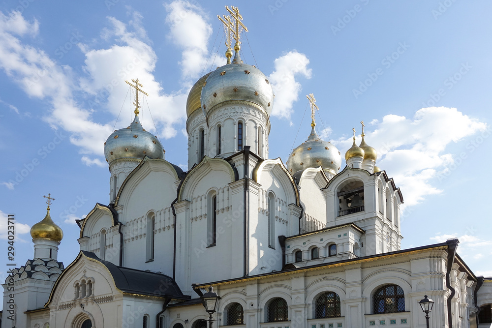 Golden domes with crosses of an orthodox temple on the background of bright blue sky. Snow-white facade. Christian faith.
