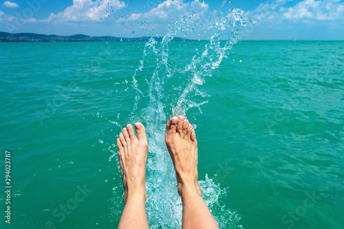 A happy girl woman is kicking feet on a sea lake and splashing water on a sail boat summertime