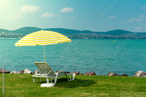 Fotografie, Obraz Stylish lounger plastic sunbed with yellow stripes sunshade beach umbrella on the green grass on beach at summer under open sky