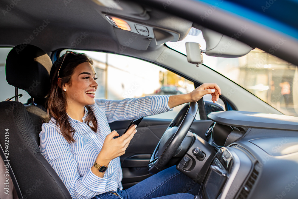 Portrait of a young woman texting on her smartphone while driving a car. Business woman sitting in car and using her smartphone. Mockup image with female driver and phone screen