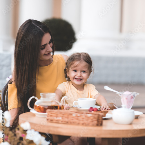Happy mother with kid daughter girl 2-3 year old eating cakes in cafe on breakfast outdoors. Good morning. Motherhood. Childhood.