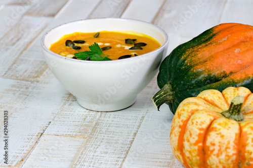 organic pumpkin soup in a white bowl framed by pumpkins photo