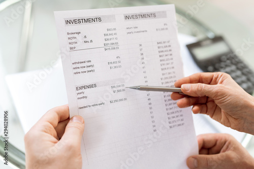 Human hand holding pen while pointing at sum of money in financial document