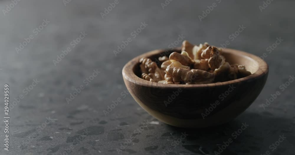 Slow motion peeled walnut kernels falling into wooden bowl on terrazzo countertop Slow motion peeled walnut kernels falling into wooden bowl on terrazzo countertop