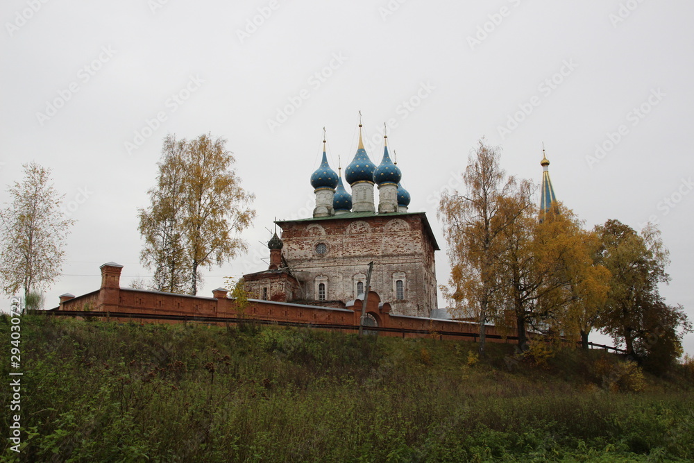 Fototapeta premium Old church in russia among yellow birch trees in cloudy day