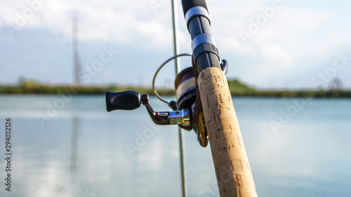 Fishing on a beautiful lake. Fishing rod, fishing line and tackle close-up. Green forest and blue sky in the background..