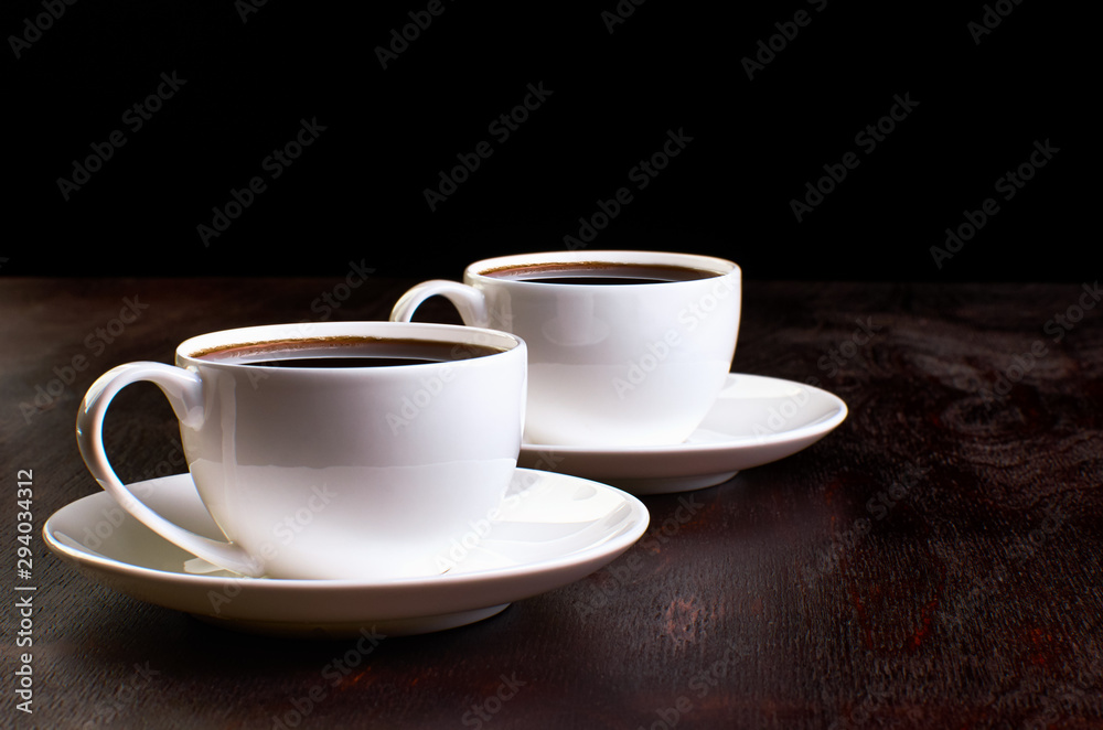 Two cups of coffee in saucers on a dark wooden table.