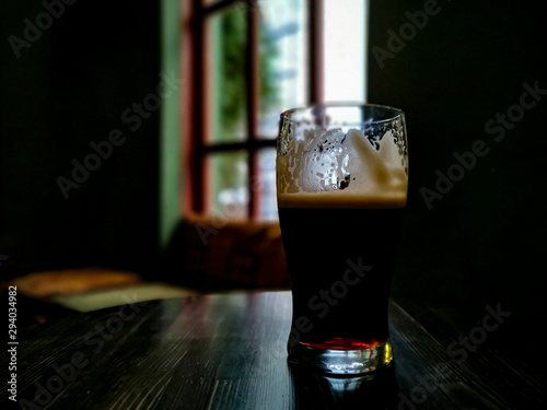 Tableau sur toile Irish stout in a pint glass on a dark wooden table – beer is half drunk, light s