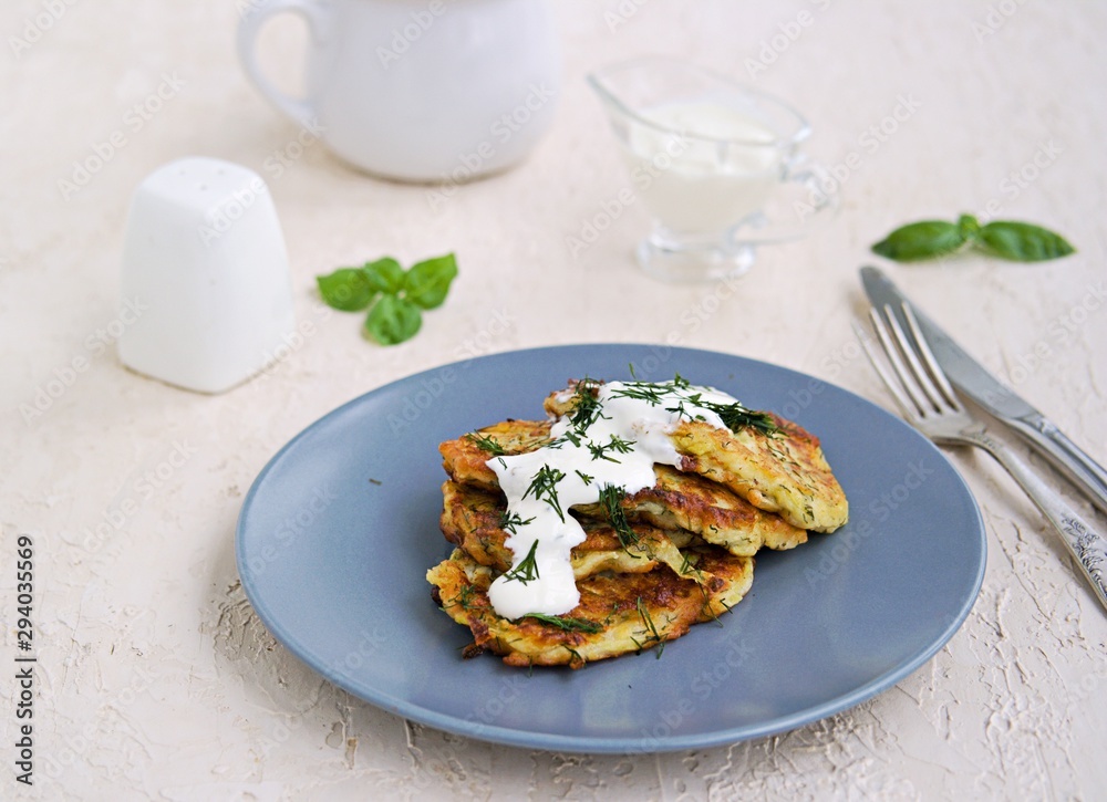 Fritters zucchini with feta cheese on a gray plate on a light concrete background. Served with sour cream. Zucchini recipes. Selective focus. Fritters zucchini with feta cheese on a gray plate on a light concrete background. Served with sour cream. Zucchini recipes. Selective focus.