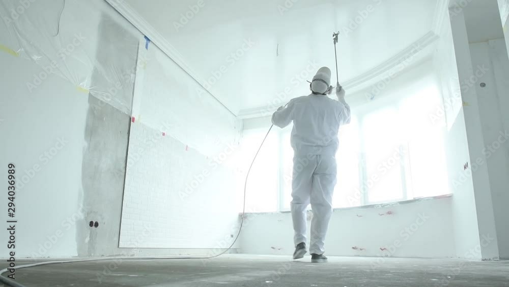 Painter works with airless spray gun when painting ceiling