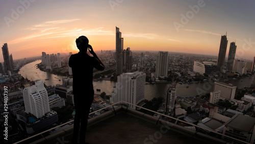 Businessman standing using smart phone on open roof top balcony watching city night view.Business with ambition and vision concept.