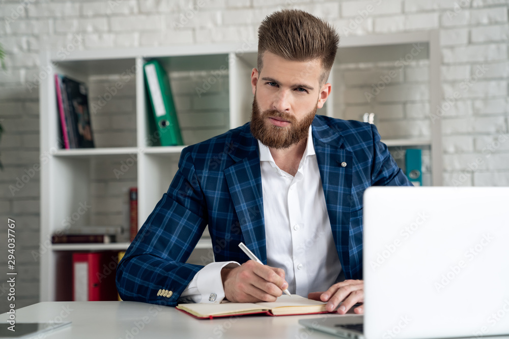 Entrepreneur writing notes sitting at his desk. Young man making business plans with papers and computers on his desk.