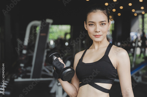 athletic young asian pretty slim body woman exercise with dumbbell in fitness gym with machine in background, bodybuilder, healthy lifestyle, exercise fitness, workout and sport training concept