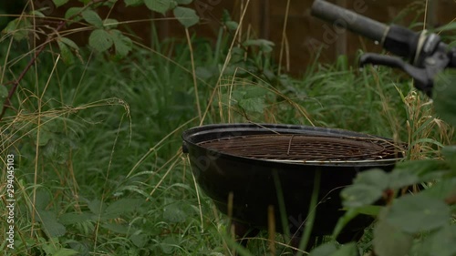 Overgrown garden with rusty BBQ and bike handle in the rain