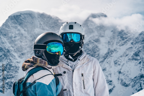 snowboarders girl and guy, close-up on the background proudly, looking at the camera, wearing blue snowboard glasses that reflect the mountains