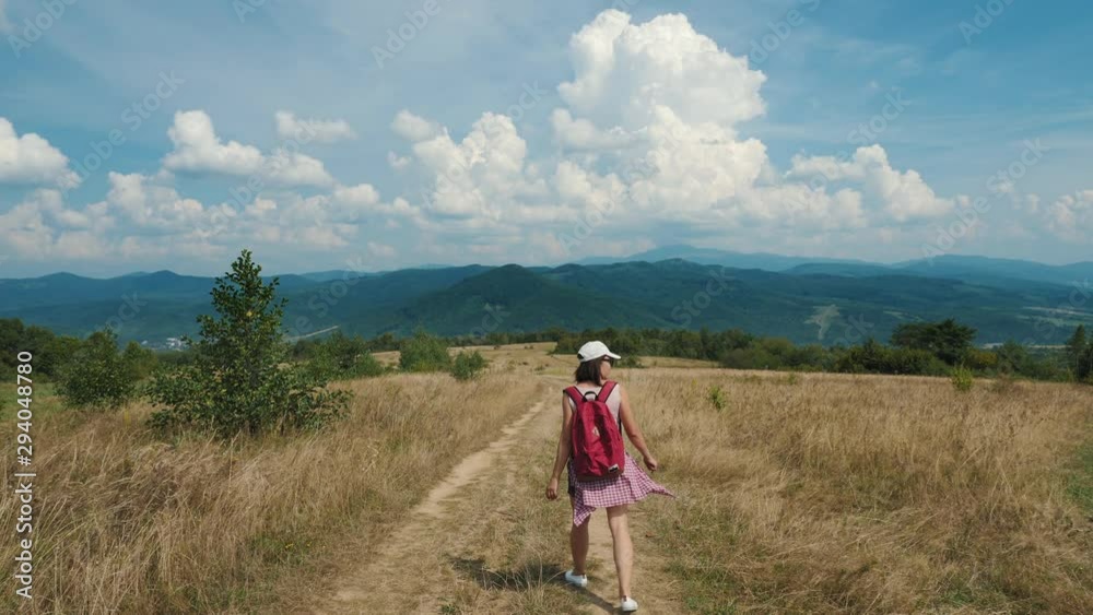 Woman traveler with a red backpack is walking on a mountainous area on a warm sunny summer day. Woman traveler with a red backpack is walking on a mountainous area on a warm sunny summer day.