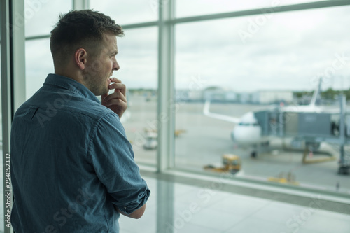 Caucasian young man is afraid to flight standing in terminal near window photo