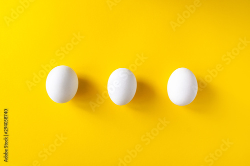 Three white eggs on a yellow background. International world egg day concept