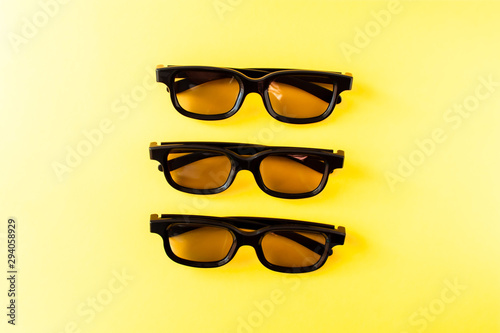 View from above of three pairs 3D black glasses on yellow background. Flat lay, cinema concept