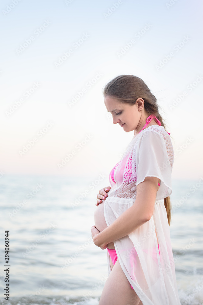Young pregnant woman is standing on the seashore and hugging her belly. Enjoying the moment. Young pregnant woman is standing on the seashore and hugging her belly. Enjoying the moment.