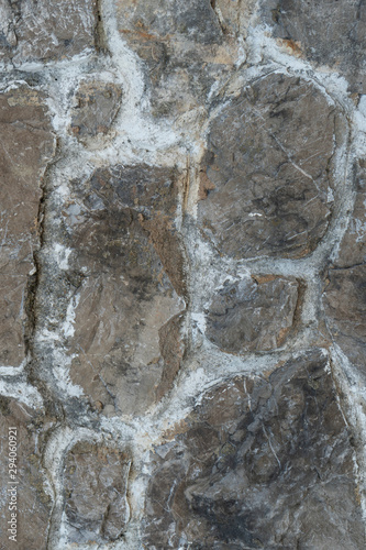 Old gray-black wall made of natural stones with wide cement joints. Gloomy abstract background